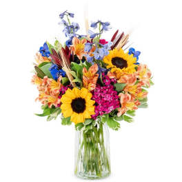 Mixed bouquet with sunflowers, blue flowers, and orange blooms in a clear glass vase