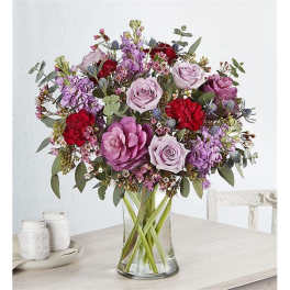 Mixed bouquet of pink, purple, and red flowers in a clear glass vase