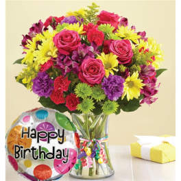 Mixed bouquet of pink roses, yellow daisies, and purple flowers in a glass vase with a birthday balloon.