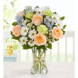 Bouquet of peach roses, white daisies, and blue flowers in a clear glass vase