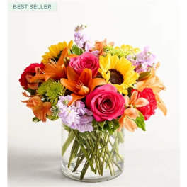 Mixed bouquet of roses, sunflowers, lilies, and carnations in a clear glass vase
