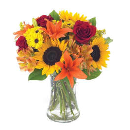 Bouquet of sunflowers, red roses, and orange lilies in a clear glass vase