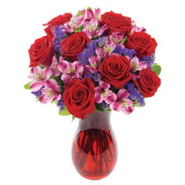 Red roses and pink flowers arranged in a red glass vase