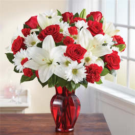 Red roses, white lilies, and daisies arranged in a red glass vase