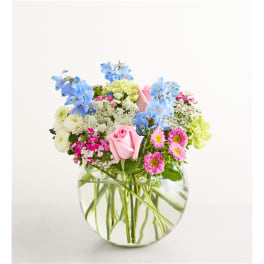 Mixed bouquet of pink, blue, and white flowers in a clear glass vase