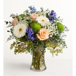 Mixed bouquet of peach roses, white gerbera daisies, and blue flowers in a glass vase