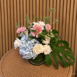 Pink gerbera daisies, white roses, and blue hydrangeas in a glass vase