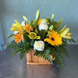 Mixed bouquet in a wooden basket with yellow lilies, white roses, and orange alstroemeria