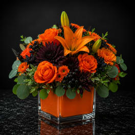 Orange roses and lilies in a square glass vase