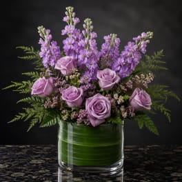 Lavender roses and purple flowers arranged in a glass vase