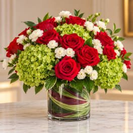 Red roses and white flowers arranged in a glass vase with green hydrangeas