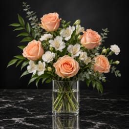 Peach roses and white flowers arranged in a clear glass vase