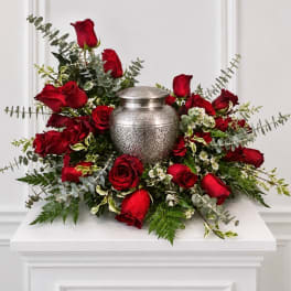 Red roses arranged around a silver urn on a white pedestal