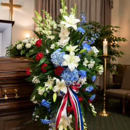 Standing funeral spray with white lilies, blue hydrangeas, and red carnations
