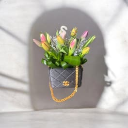 Tulips arranged in a black quilted handbag with a gold chain