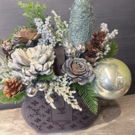 Holiday arrangement with pinecones, silver ornaments, and a dark monogrammed bag