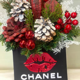 Holiday arrangement with pinecones, red berries, and a Chanel gift bag