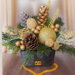 Holiday arrangement with pinecones, gold ornaments, and evergreen in a black handbag-shaped container