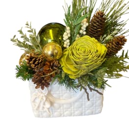 Holiday arrangement with a green flower, pinecones, and ornaments in a white vase