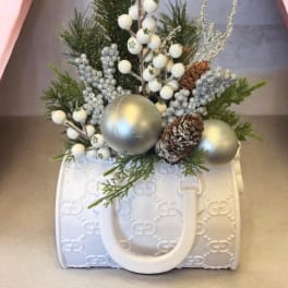 Holiday arrangement in a white patterned handbag-shaped container with silver ornaments and pinecones