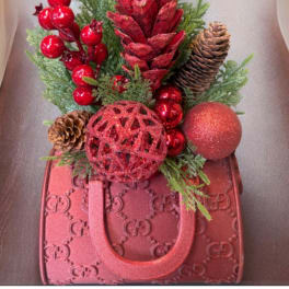 Red holiday arrangement with pinecones and ornaments in a red handbag