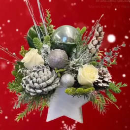 Christmas arrangement with white roses, pinecones, and silver ornaments in a star-shaped container