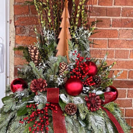 Christmas arrangement with pinecones, red ornaments, and ribbon on a wooden tree form
