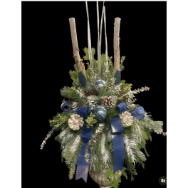 Holiday arrangement with pine, blue ribbons, and silver ornaments in a container