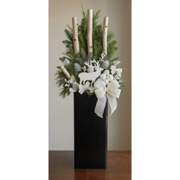 Winter arrangement with evergreen branches, birch stems, and a white reindeer ornament in a black vase