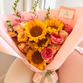 Bouquet of sunflowers, roses, and pink snapdragons wrapped in peach paper