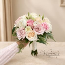 Pink and white rose bridal bouquet with greenery, held by a hand
