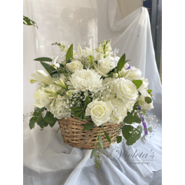 White floral arrangement in a wicker basket with roses and lilies