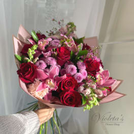Handheld bouquet of red roses and pink orchids wrapped in blush paper