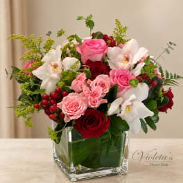 Pink and red roses with white orchids in a clear square vase