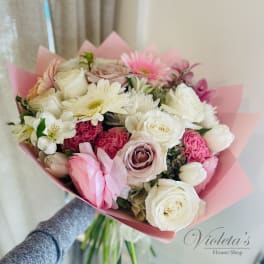 Handheld bouquet of pink and white roses with mixed blooms wrapped in pink paper