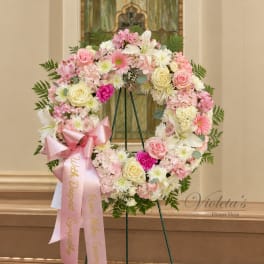 Pink and white floral wreath on a stand with a pink ribbon bow