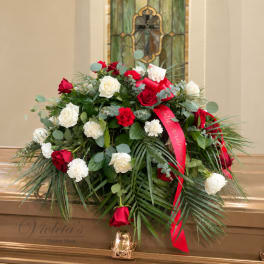 Red and white roses arranged in a casket spray with a red ribbon