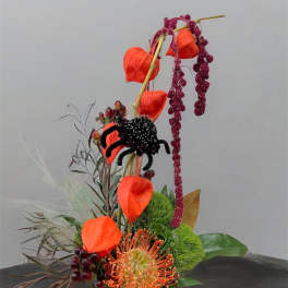 Tall floral arrangement with orange and black blooms in a low dark container