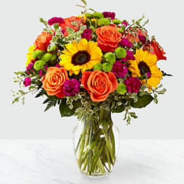 Bouquet of orange roses and yellow sunflowers in a clear glass vase