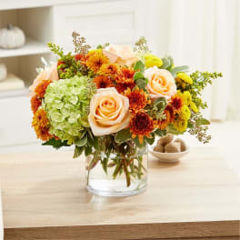 Peach roses and orange chrysanthemums in a clear glass vase