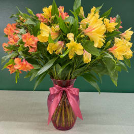 Bouquet of yellow and coral alstroemeria in a pink glass vase with a ribbon