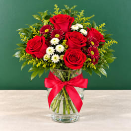 Red roses and small white flowers in a glass vase with a red ribbon