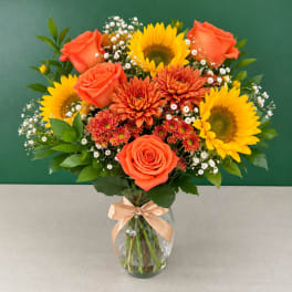 Bouquet of orange roses, sunflowers, and chrysanthemums in a glass vase