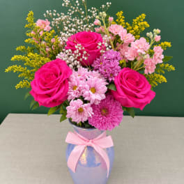 Pink roses and mixed blooms in a blue vase with a pink ribbon