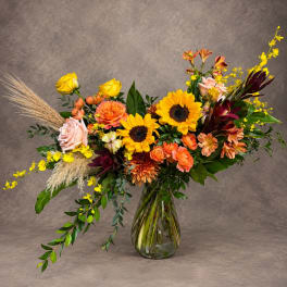 Mixed bouquet with sunflowers, roses, and orange blooms in a glass vase