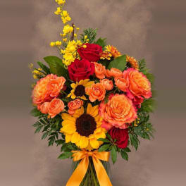 Bouquet of red roses, orange blooms, and yellow sunflowers in a glass vase