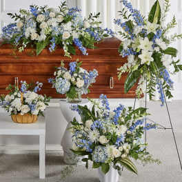 Blue and white floral funeral arrangements around a wooden casket