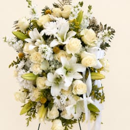 White floral standing spray with roses, lilies, and daisies on a ribboned easel