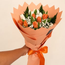 Handheld bouquet of orange and white tulips wrapped in peach paper