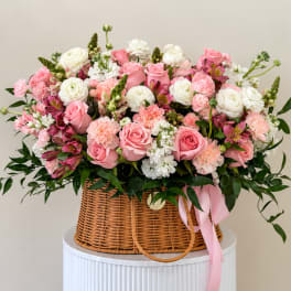 Pink and white flower arrangement in a wicker basket with a pink ribbon